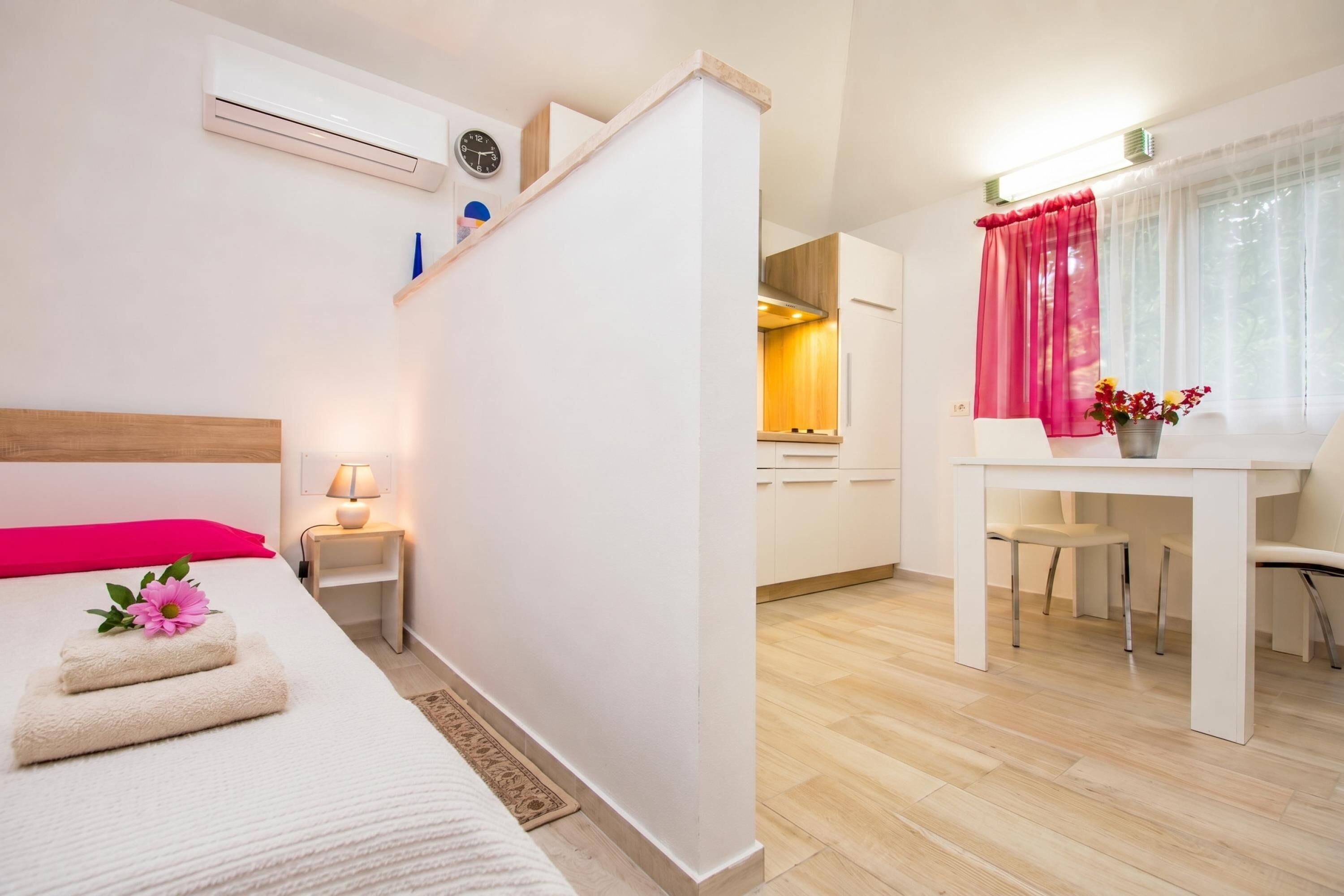 A hotel room with a bed, bedside table, lamp, and a view into the kitchen area.