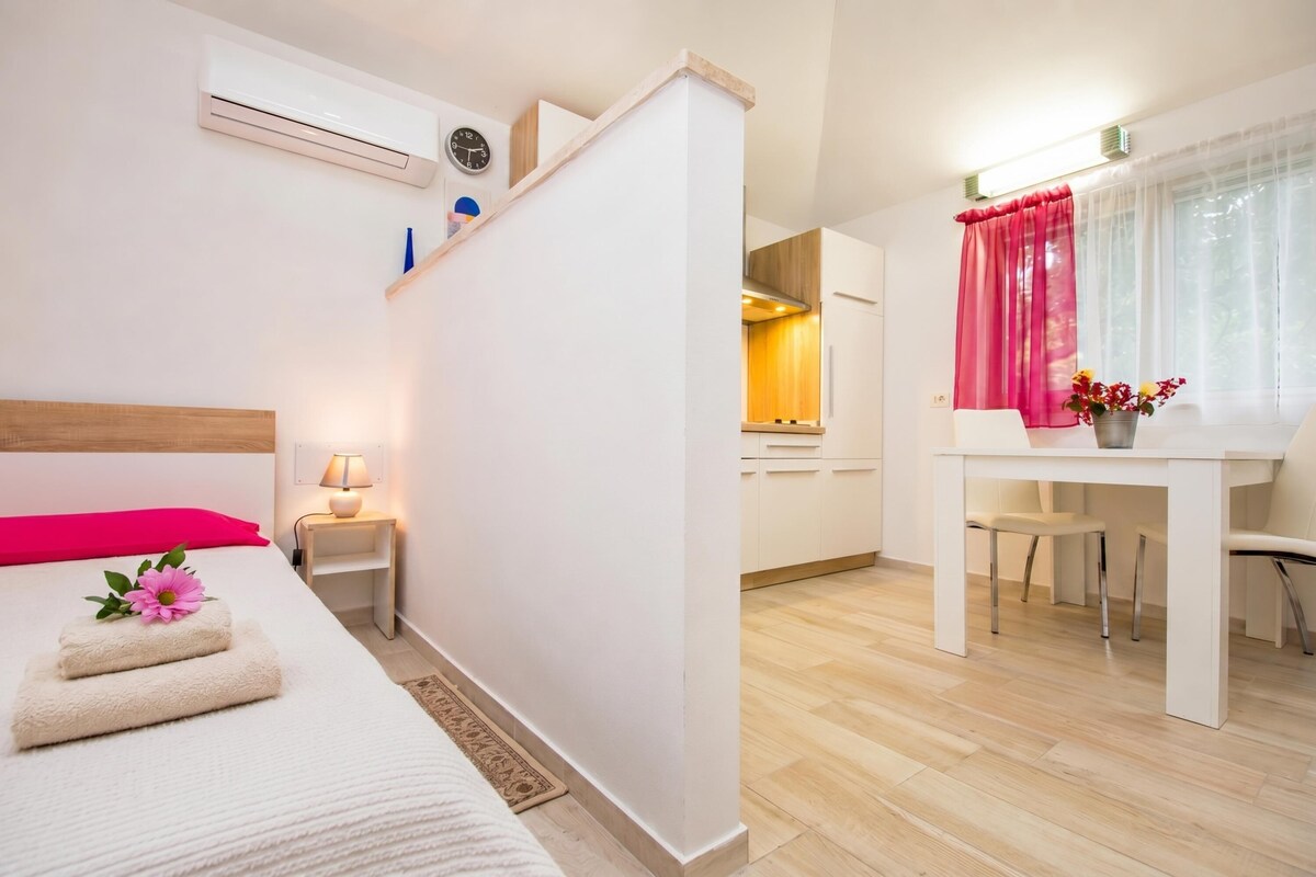 A hotel room with a bed, bedside table, lamp, and a view into the kitchen area.
