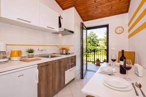 A modern kitchen with a dining area, a view of the garden, and a clock on the wall. - Marisa Olive Grove Apartments (Labin)