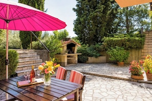 An outdoor patio with a wooden table, chairs, a pink umbrella, and potted plants. - Marisa Olive Grove Apartments (Labin)