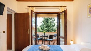 A bedroom with a bed, a window, a door, a table with chairs, and a potted plant outside. - Marisa Olive Grove Apartments (Labin)