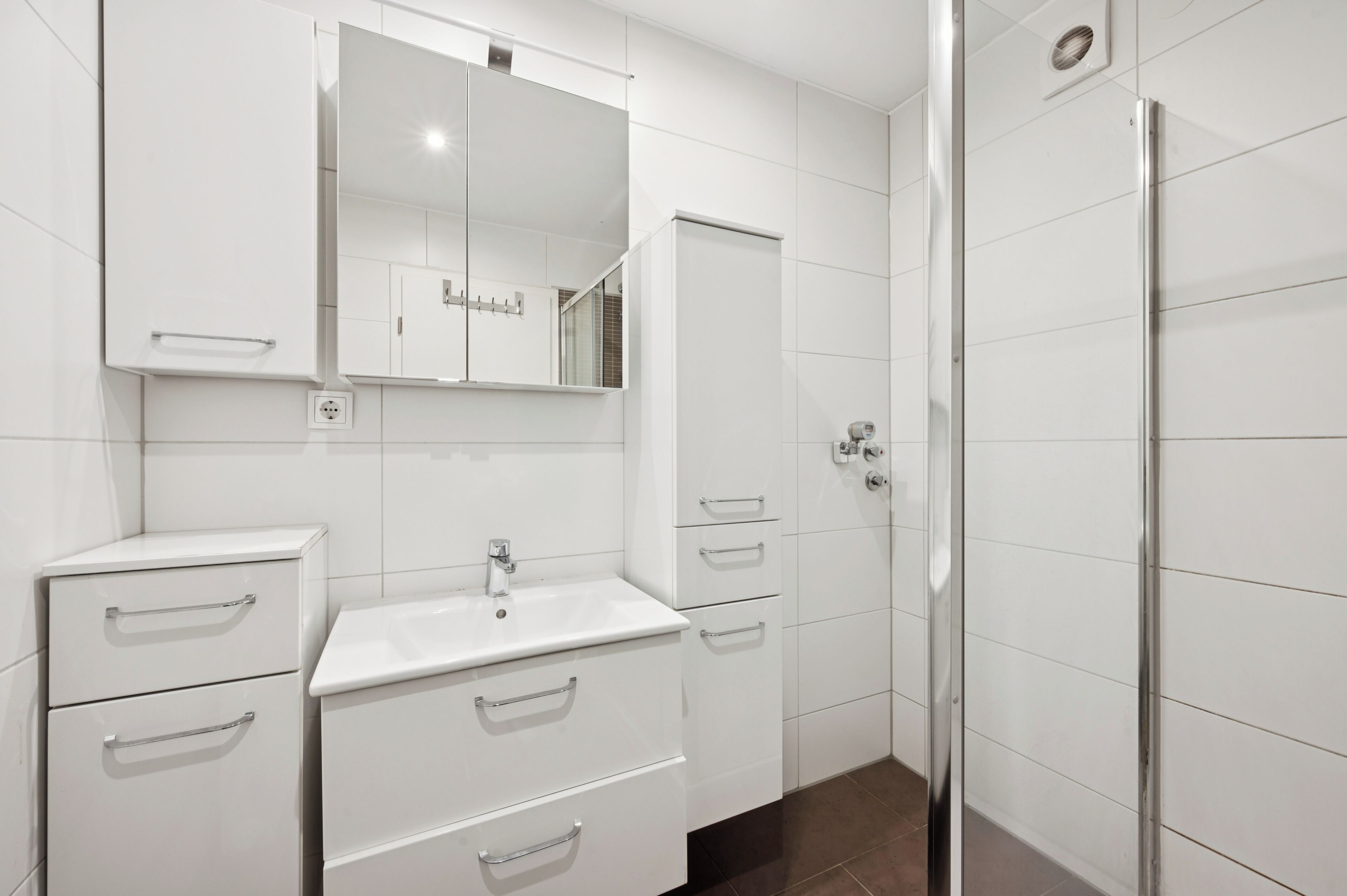 A modern bathroom with white cabinetry, a mirror, a sink, and a shower enclosure.