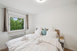 Ein Schlafzimmer mit großem Fenster, einem Bett mit gestreifter Bettwäsche und einem Nachttisch mit Lampe.