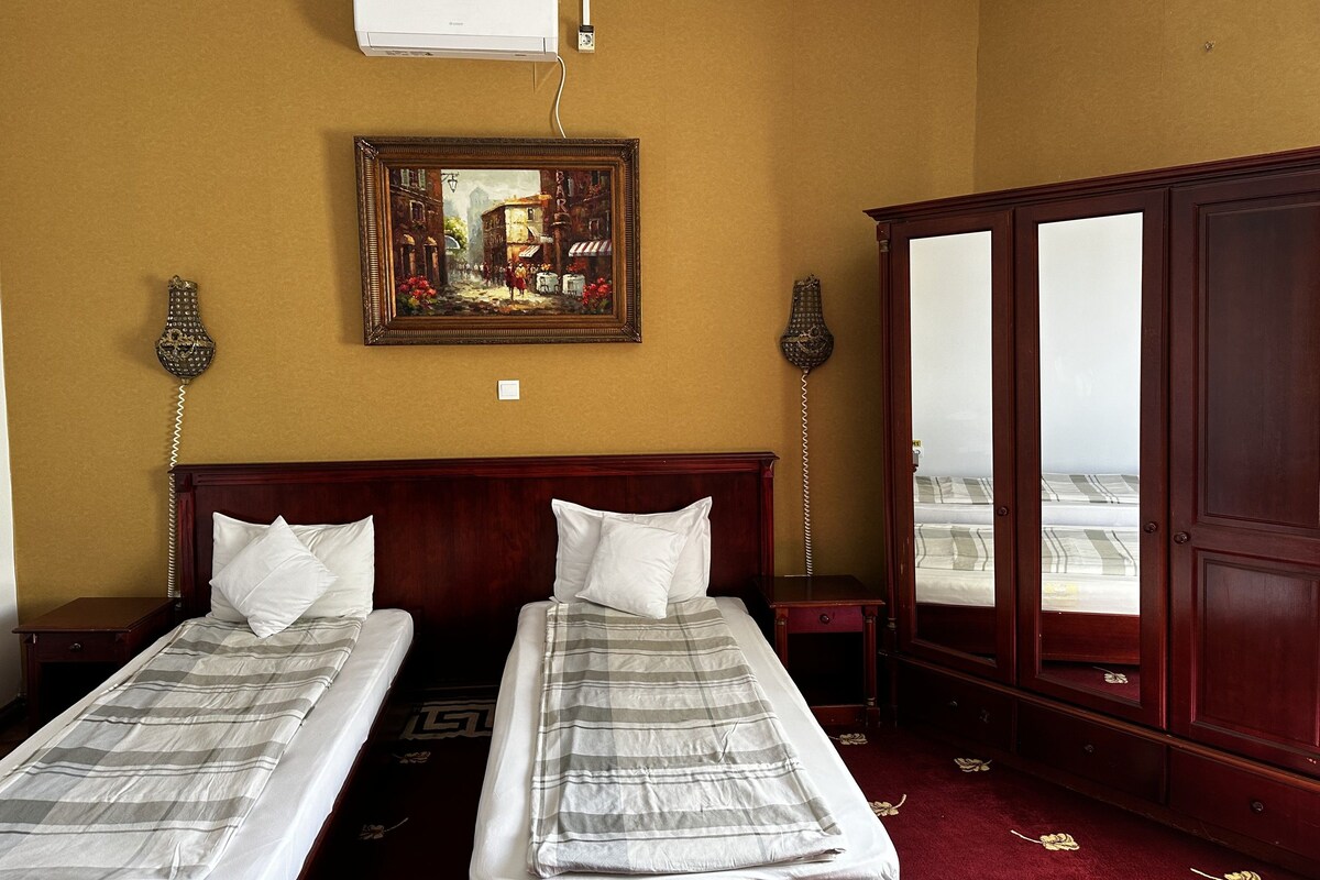 A hotel room with two beds, a painting on the wall, an air conditioning unit, and a wardrobe.