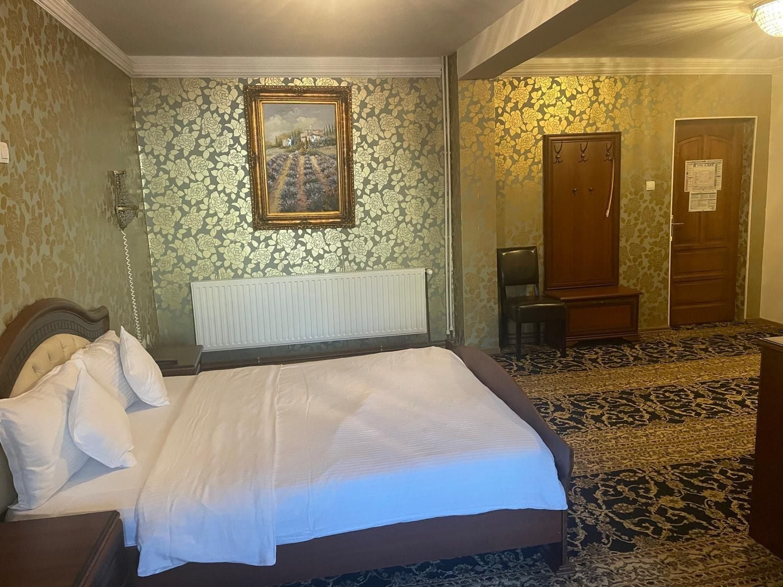 Una habitación de hotel con cama, radiador, puerta de madera y alfombra estampada.