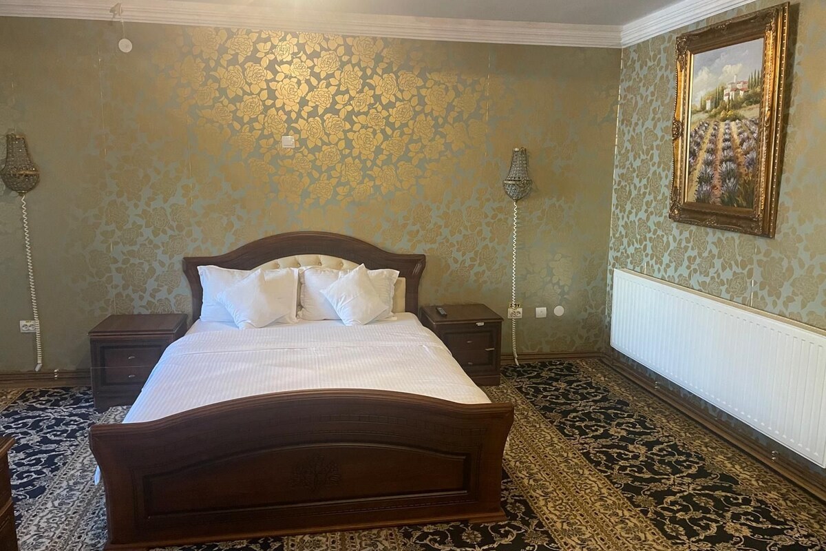 A bedroom with a large bed, two bedside tables, a wall-mounted lamp, and a framed picture.