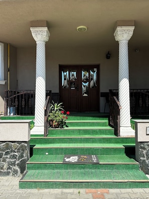 Entrada de un edificio con puertas dobles, dos columnas y una escalera alfombrada de color verde.