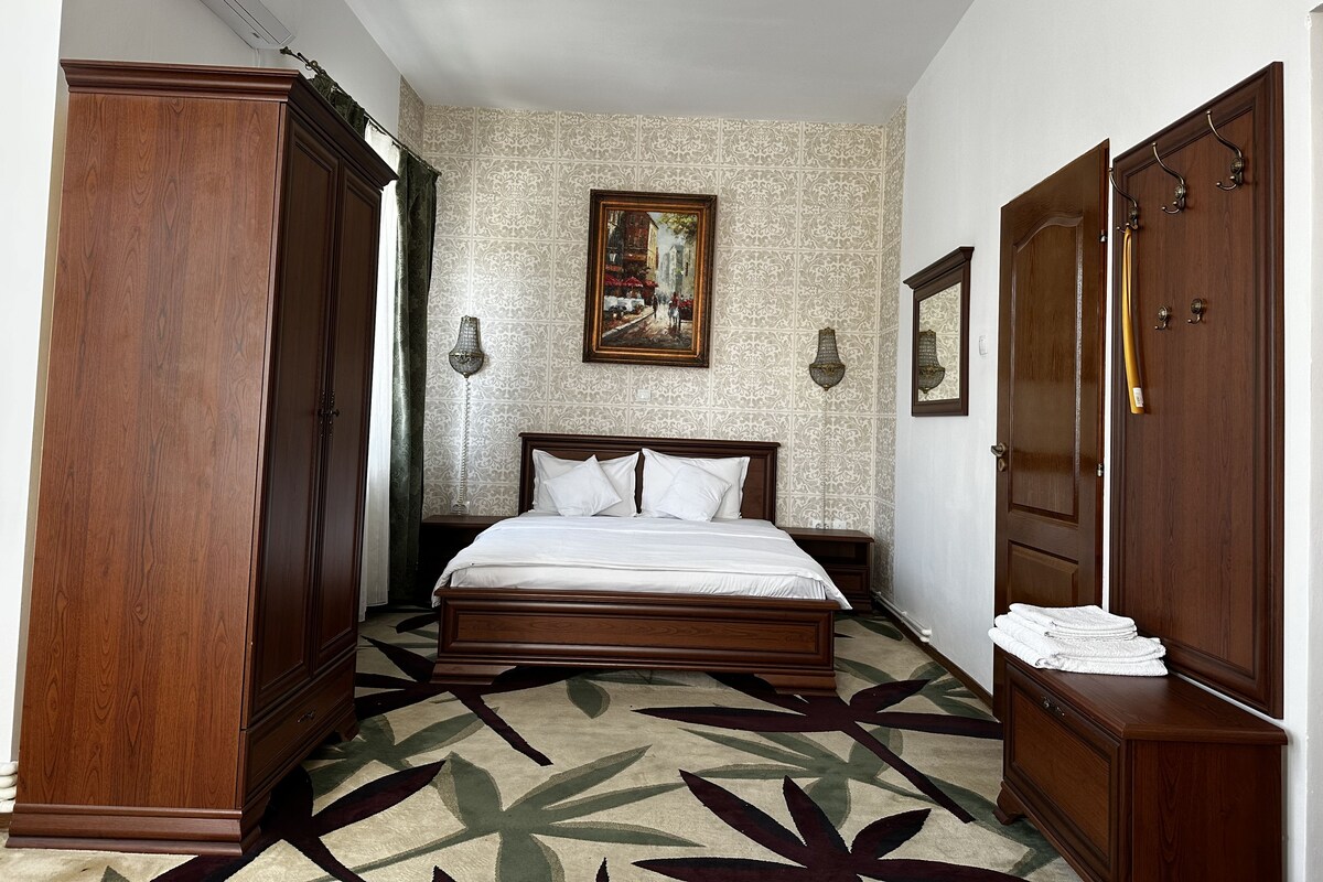 A bedroom with a large bed, wooden wardrobe, and a painting on the wall.