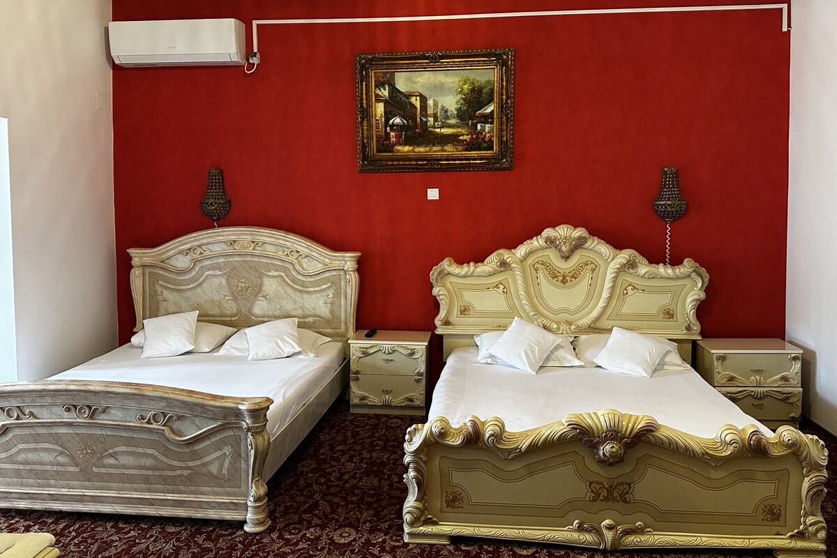 A hotel room with two beds, a red wall, and a painting.