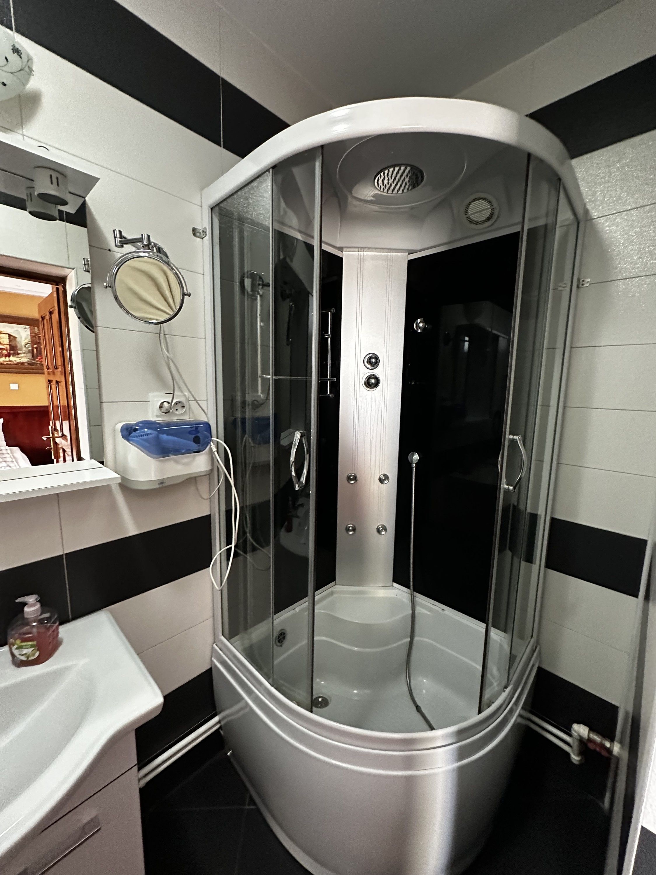 A corner shower with a glass enclosure, a sink with a blue basin, and a mirror above the sink.