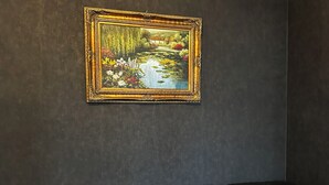 A dark wall with a framed painting of a garden scene and a black leather sofa. - CROWN ROYAL APARTMENTS (Alba Iulia)