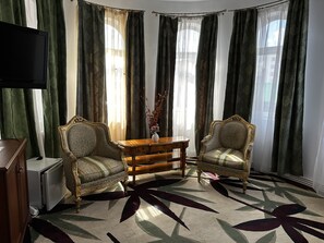 Una habitación con dos sillones decorativos, una mesita de madera, un televisor y una alfombra estampada.