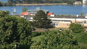 A building with a flat roof, a parking area, and a view of a body of water. - Beautiful vacation rental in Heiligenhafen with ocean view + balcony through Oct. 2026 (Heiligenhafen)