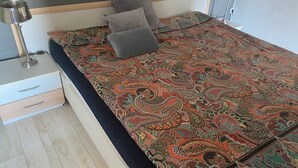 A neatly made bed with a patterned bedspread, two bedside lamps, a drawer unit, and a wooden headboard. - Beautiful vacation rental in Heiligenhafen with ocean view + balcony through Oct. 2026 (Heiligenhafen)