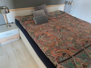 Un lit bien fait, avec une couvre-lit à motifs, deux lampes de chevet, une commode et une tête de lit en bois.