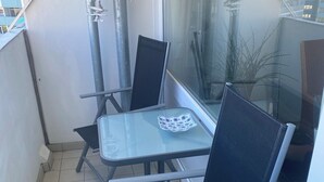 A corner of a room with a glass table and two chairs, a potted plant, and a window with a view of buildings. - Beautiful vacation rental in Heiligenhafen with ocean view + balcony through Oct. 2026 (Heiligenhafen)