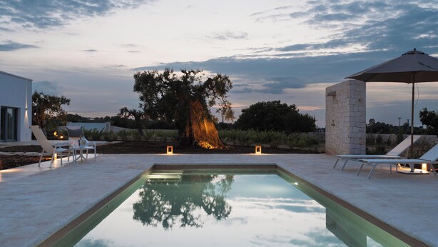 A swimming pool with lounge chairs and an umbrella, surrounded by a landscaped garden and a modern building. - Trulli Vigna Lamafico Suites & Pool (Polignano a Mare)