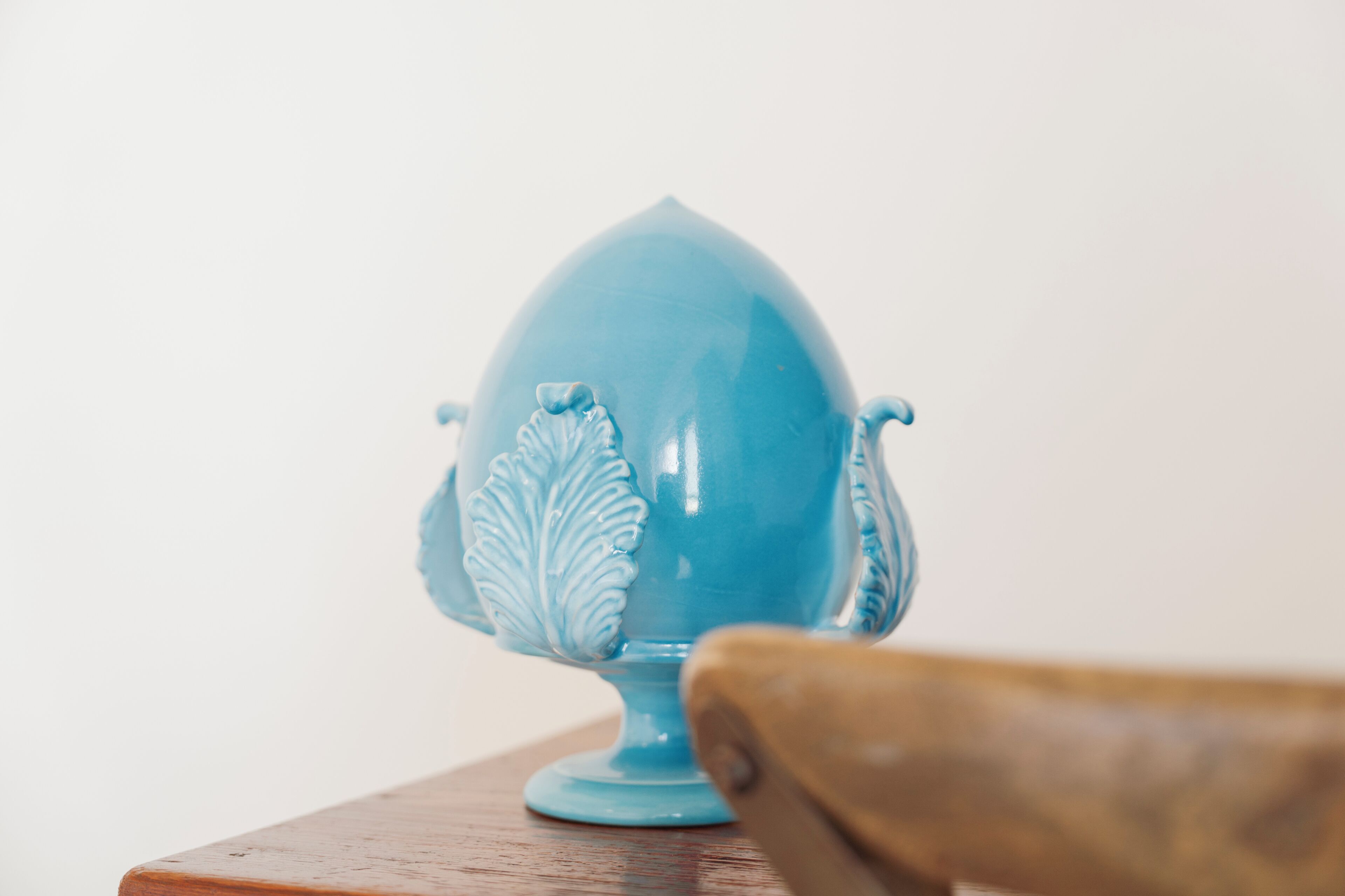 Een blauw keramieken object met een bladmotief op een houten ondergrond.