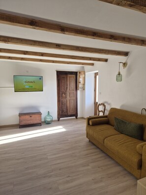 A living room with a wooden floor, a sofa, a television, and a wooden door. - Traditional house (Figari)