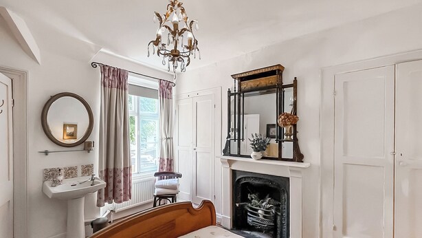 A bedroom with a bed, a fireplace, a mirror, a window with curtains, and a chandelier. - 3 bedroom accommodation in Torquay (Torquay)