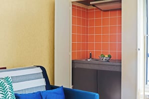 Ein gemütlicher Wohnbereich mit Küchenzeile, einem blauen Sofa mit gestreiften Kissen und einem kleinen Fenster.