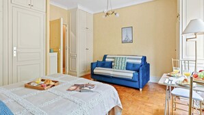 Ein Zimmer mit einem Bett, einem blauen Sofa, einem Esstisch mit Frühstück und einer Kandelaber.