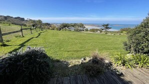 Ett grönområde utomhus med en träaltan, utsikt över havet och några träd.