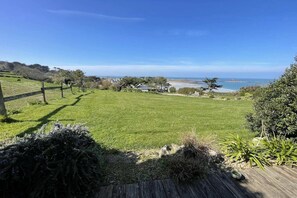 A grassy outdoor area with a wooden deck, a view of the ocean, and some trees. - Cozy Detached Rental for 2 (Plougasnou)