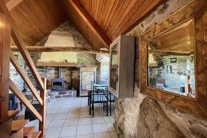 A rustic interior with a stone wall, wooden ceiling, a fireplace, and a dining area with a table and chairs. - Cozy Detached Rental for 2 (Plougasnou)
