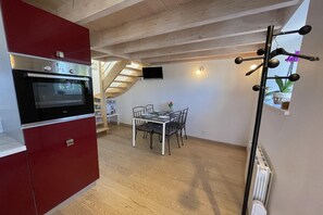 A kitchen with a red cabinet, a built-in oven, and a dining area with a table and chairs. - Rental for 2 with Private Outdoor Space (Plougasnou)