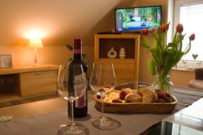 A dining table with a bottle of wine, two glasses, a bowl of fruit, and a vase of tulips. - MS Apartments | Sielterrasse 2 (Ditzum)