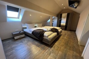 A modern bedroom with a loft-style ceiling, a bed with white linens, a nightstand, and a wooden floor. - MS Apartments | Sielterrasse 2 (Ditzum)