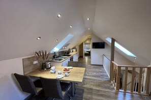 A modern kitchen with a dining area, wooden flooring, and a staircase leading to an upper level. - MS Apartments | Sielterrasse 2 (Ditzum)