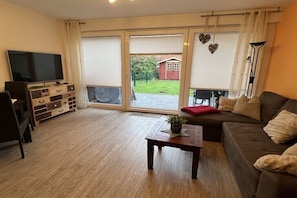 Ein Wohnzimmer mit einer Couch, einem Couchtisch, einem Fernseher und einer Glastür, die zu einem Garten führt.