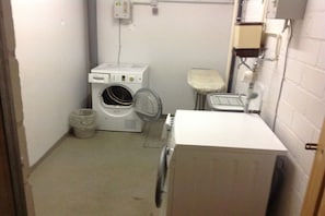 A compact laundry room with a front-loading washer, a stacked dryer, and a small trash bin. - Holiday apartment with 1 bedroom (Cuxhaven-Döse)