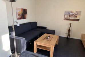A modern living room with a grey sectional sofa, a wooden coffee table, a floor lamp, and two wall art pieces. - Holiday apartment with 1 bedroom (Cuxhaven-Döse)