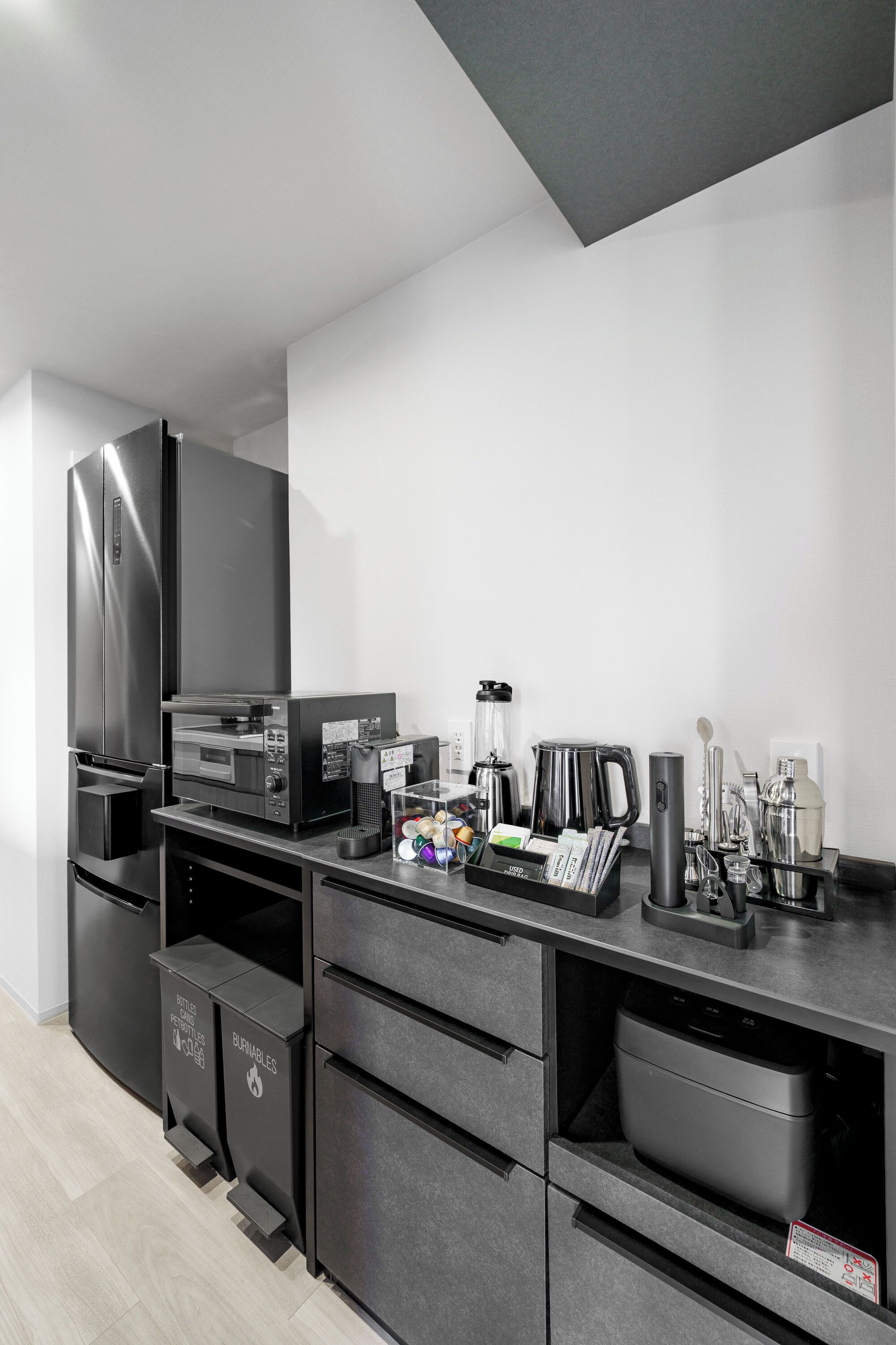 Eine moderne Küche mit Einbauofen, Mikrowelle und Kaffeemaschine. Es sind schwarze Schränke und eine Arbeitsplatte mit verschiedenen Geräten und Kochutensilien zu sehen.