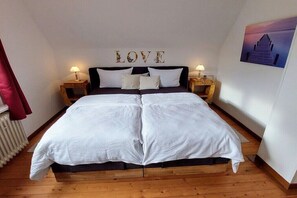 A double bed with white bedding, two bedside tables with lamps, a wall-mounted word 'LOVE', and a painting of a staircase. - Holiday home in Norden with swimming pool (Norden)