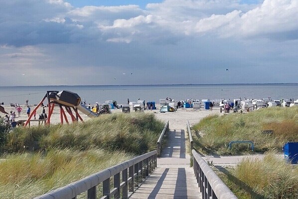 A beach with a wooden walkway leading to the water, a telescope, and people enjoying the beach. - Holiday home in Norden with swimming pool (Norden)
