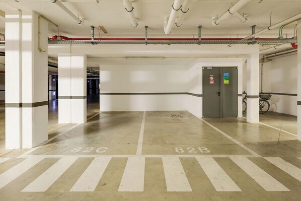 A parking garage with white pillars, marked parking spaces, and a fire extinguisher on the wall. - The Prestige The Vilamoura Residences (Loulé)