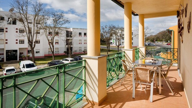 A balcony with a view of a building, a green fence, and a table with chairs. - Central Albufeira Stay Balcony AC (Albufeira)
