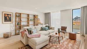 En moderne stue med sofa, sofabord og udsigt til bybilledet gennem store vinduer.