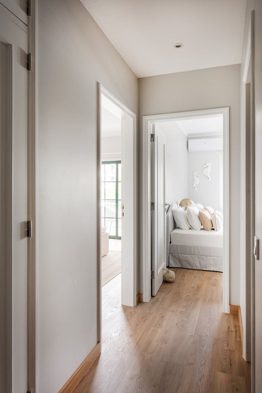 A hallway leading to a bedroom with a bed, a window, and a door.