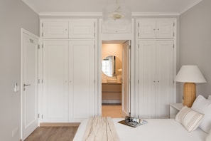 A bedroom with a bed, a bedside lamp, a mirror, and a wardrobe. - Carcavelos Terrace Beach Apartment (Cascais)