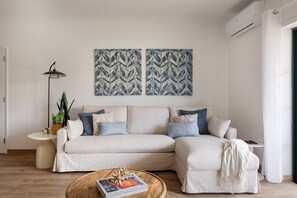 Una sala de estar con un sofá, una mesita de centro, una lámpara de pie y dos obras de arte colgadas en la pared.