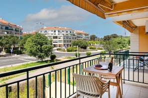 A balcony with a table and chairs, overlooking a street with buildings and greenery. - Carcavelos Terrace Beach Apartment (Cascais)