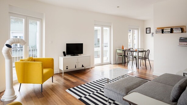 A modern living room with a sofa, a yellow chair, a TV, a dining area with chairs, and a bookshelf. - Estrela Skyline Retreat With Terrace (Lisbon)