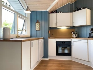 A kitchen with white cabinets, a black oven, and a window with a view of greenery. - Bright holiday home with large terrace near Nyborg (Nyborg)