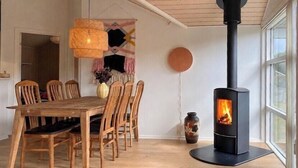Ein Essbereich mit einem Holztisch und Stühlen, einem schwarzen Herd mit Feuer und einer hängenden Lampenschirm aus Bändern.