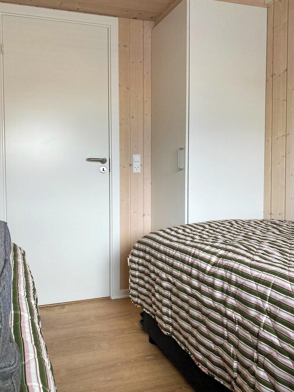 A bedroom with a bed, a door, and a wooden floor.